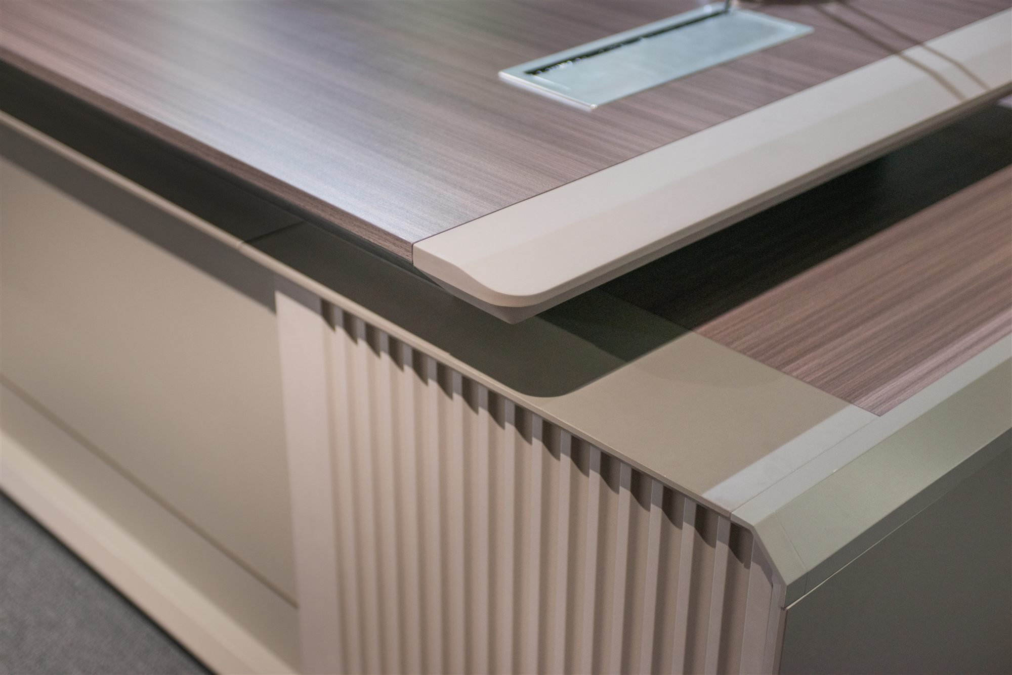 Desk edge detail: veneer top, metal trim and cable grommet